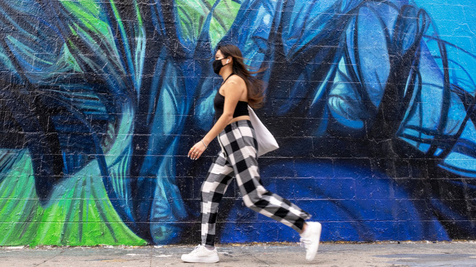 LOS ANGELES, CALIFORNIA - APRIL 22: A woman wearing a mask walks past a mural advertising Billie Eilish's 'The Worlds A Little Blurry' on Apple TV on Melrose Avenue amid the coronavirus pandemic on April 22, 2021 in Los Angeles, California. Los Angeles County moved into Covid-19 orange tier restrictions on April 5 allowing increased capacity at restaurants, movie theaters and museums. (Photo by Alexi Rosenfeld/Getty Images)